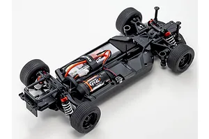 Top-down studio shot of the unpainted chassis of the Kyosho Fazer MK2 FZ02L RC car, showing electronics, motor, and suspension against a white background.