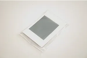 Photo-etched metal mesh sheet inside a protective plastic bag on a white surface.