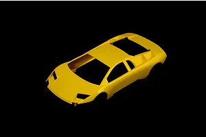Unassembled yellow plastic model car body shell for a Lamborghini Murcielago against a black background.