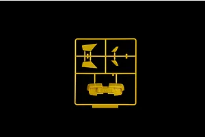 Yellow plastic model kit sprue containing car parts including a rear bumper and wing sections against a black background.