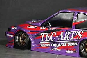 Close-up side view of a purple RC drift car body featuring Tec-Art's sponsor decals and gold mesh wheels.