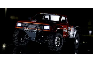 Kyosho Outlaw Renegade 2WD short course RC truck in red and black with illuminated headlights parked outside at night.