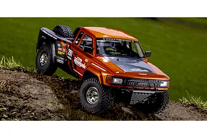 Kyosho Outlaw Renegade RC short course truck outdoors on a dirt mound, featuring a metallic orange and black body.