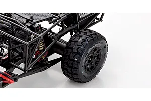 Close-up of the rear suspension and knobby tire on a Kyosho Outlaw Renegade 1/10 scale RC short course truck against a white background.