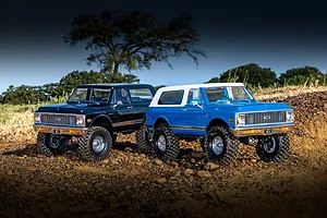 Two Traxxas TRX-4 Chevrolet Blazer RC rock crawlers in black and blue parked outdoors on rocky terrain.
