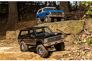 Two Traxxas TRX-4 Chevrolet Blazer RC rock crawlers in black and blue parked on rocky terrain outdoors.