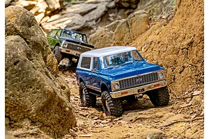 Two Traxxas TRX-4 Chevrolet Blazer RC rock crawler trucks navigating a rocky dirt trail outdoors.