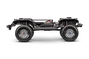 Side view of the bare Traxxas TRX-4 RC crawler chassis without body shell, showing frame rails, suspension, and wheels against a white background.