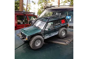 Axial SCX10 III Jeep Cherokee XJ RC rock crawler parked on the hood of a real full-size vehicle outdoors.