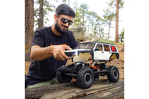 Man adjusting the white body of an Axial SCX10 III Jeep Cherokee XJ RC rock crawler outdoors on a log.