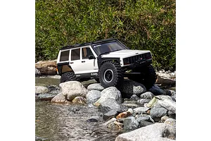 Axial SCX10 III Jeep Cherokee XJ RC rock crawler driving over river rocks in an outdoor setting.