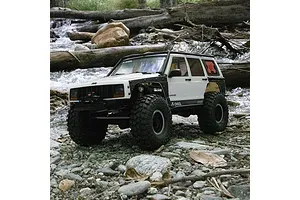Axial SCX10 III Jeep Cherokee XJ RC rock crawler driving on rocky ground beside a stream outdoors.