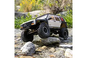 Axial SCX10 III Jeep Cherokee XJ RC rock crawler driving through a shallow rocky stream outdoors.