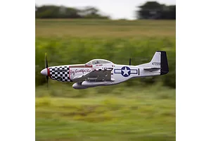 E-Flite P-51D Mustang Big Beautiful Doll RC fighter plane in flight against a blurry green field background.