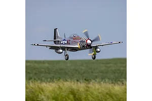 E-Flite P-51D Mustang Big Beautiful Doll RC fighter plane in flight over grassy fields with landing gear deployed.