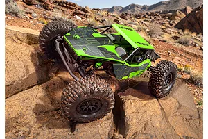 Bright green and black RC rock crawler driving over rugged desert rocks in an outdoor environment.