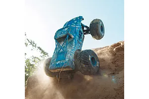 ARRMA Quake 4S RC monster truck driving vertically up a dirt embankment outdoors