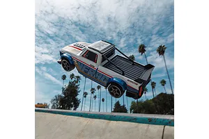 ARRMA Infraction RC truck airborne off a skate ramp against a blue sky with palm trees.