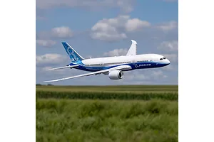 E-Flite Micro Boeing 787 Dreamliner RC airplane in flight against a cloudy blue sky and green field background.