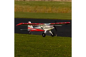 E-Flite Turbo Timber Evolution 1.5m RC plane in flight over an airfield with a red, white, and black trim scheme.