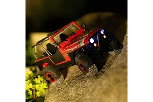 Red Axial SCX30 Jeep CJ-7 Renegade RC rock crawler driving on rocks at night with working headlights lit up.
