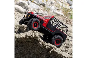 Axial SCX30 Jeep CJ-7 Renegade red RC rock crawler driving over dirt and rocks outdoors.
