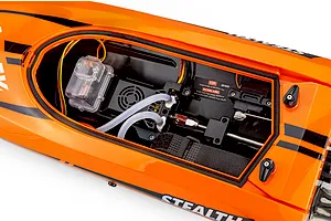 Top-down view of the interior compartment of the orange Atrek Stealth 25 RC boat, showing electronics and cooling hoses.