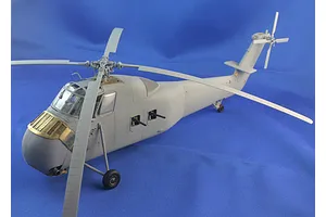 An assembled plastic model helicopter painted light grey against a blue background, showing main and tail rotors and side gun mounts.