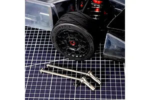 Method RC titanium CVD driveshafts and small grub screws displayed on a cutting mat in front of an RC car wheel and chassis.