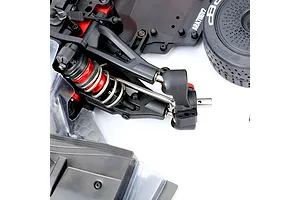 Close-up of an RC car front suspension assembly installed on a chassis, featuring a metal stub axle, shock absorber, and wheel.