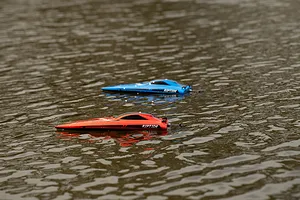Two Riptide RC speed boats, one red and one blue, floating on rippling outdoor water.