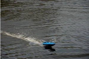 Blue and black RC speed boat running across calm dark water, creating a white wake and spray.