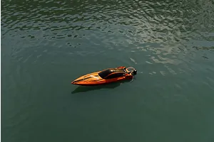An orange Atrek Rogue RC speed boat floating on calm water in an outdoor setting.