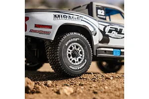 Close-up action shot of a Pro-Line RC trophy truck body shell and rear wheel on dirt terrain.