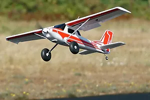 Arrows RC Bigfoot 1.3m trainer airplane in flight outdoors against a natural green and brown background