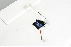 Close-up of an Arrows RC analog servo installed in white foam aircraft wing with pushrod linkage.
