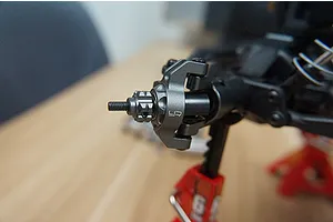 A grey aluminium steering knuckle installed on an RC car chassis, showing the Yeah Racing logo.