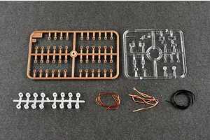 Plastic model kit parts including brown and clear sprues, small white plastic parts, copper wire, and black tubing on a grey surface.