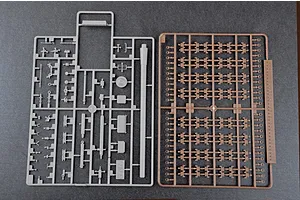 Two plastic model kit sprues on a dark grey background, one grey with various vehicle parts and one brown with track links.