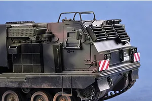 A detailed scale model of a military Mobile Artillery Rocket System (MARS) vehicle painted in camouflage green against a blue background.