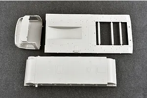 Unassembled grey plastic model kit parts for a military vehicle, including a truck cab and chassis components, viewed from above on a dark grey surface.