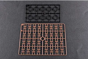 Two plastic model kit sprues on a dark grey background, one black with circular parts and one tan with small track-like components.