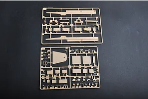 Two tan plastic model kit sprues containing various vehicle parts laid out on a dark surface.