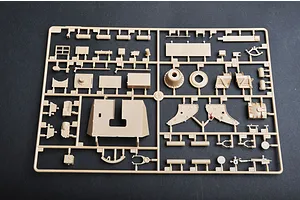 A plastic model kit sprue containing various tan-colored parts for a military vehicle model, laid out on a dark grey surface.