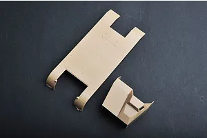 Tan plastic model kit parts for a military vehicle, including a chassis floor and cabin section, on a dark grey surface.