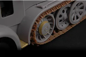Close-up of a plastic model half-track vehicle showing grey wheels, brown tracks, and gold-coloured photo-etched metal detail parts.