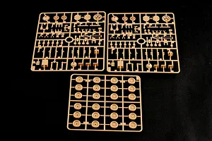 Three tan plastic model kit sprues containing various tank parts and road wheels on a black background.