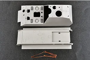 Top-down view of unpainted grey plastic model tank hull and upper chassis parts with a length of copper wire on a dark grey surface.