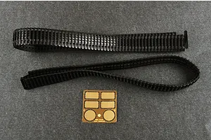 Two black plastic tank tracks and a small photo-etched brass detail sheet on a grey surface.
