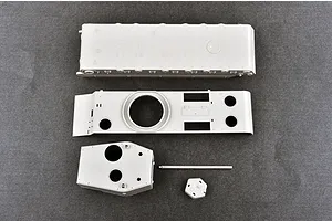 Unassembled grey plastic model kit parts for a tank, including the hull, turret, and gun barrel, laid out on a dark grey surface.